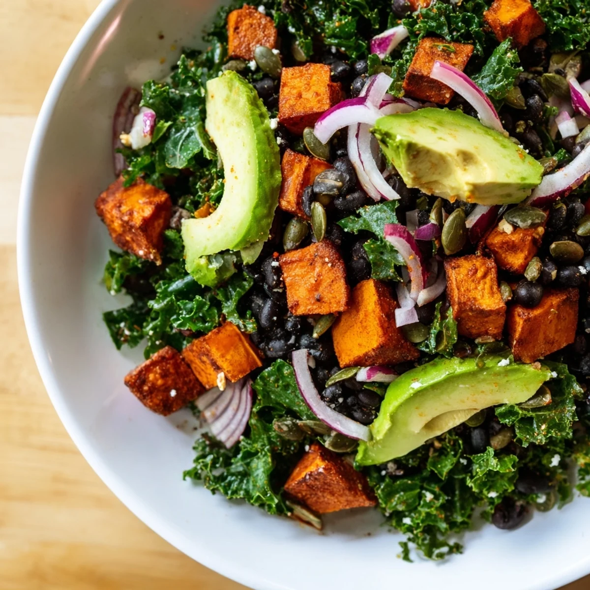 Vibrant close-up of Massaged Kale Salad with black beans, sweet potato, and creamy avocado slices.