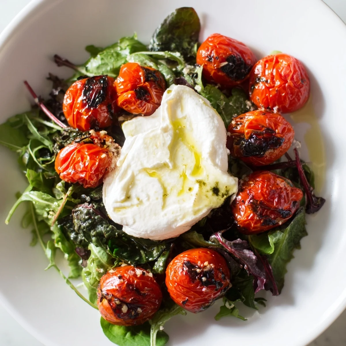 Golden-brown charred tomato salad with creamy burrata, drizzled with fragrant basil oil, a summer delight.
