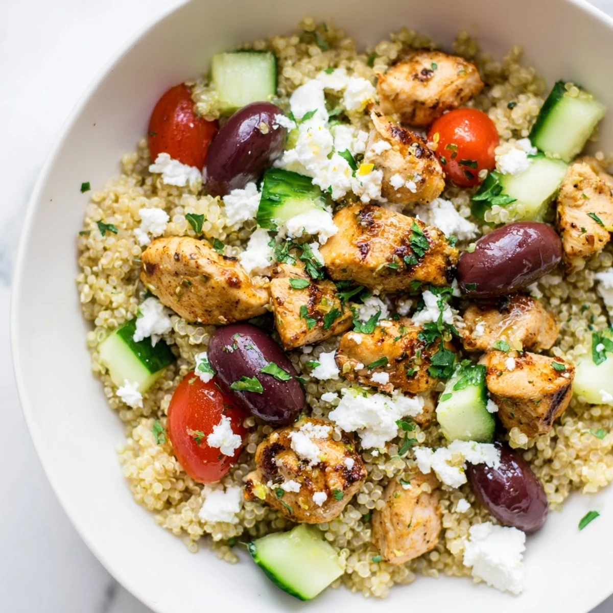 Close-up of a Mediterranean Chicken Bowl showing fluffy quinoa, crisp cucumbers, tomatoes, and crumbled feta cheese.