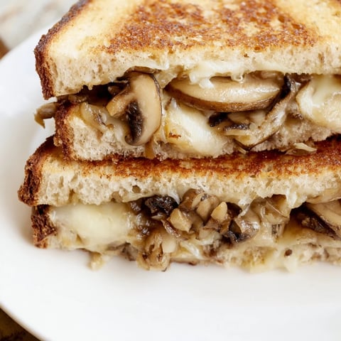 Golden-brown Mushroom Swiss Grilled Cheese sandwich on a wooden board, showing melted Swiss cheese and sautéed mushrooms oozing from between crispy rye bread slices.