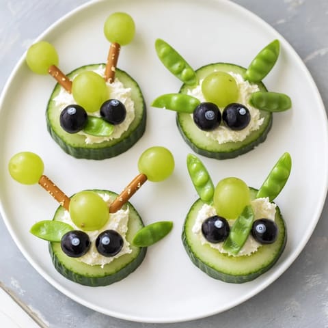 Vibrant platter of Little Green Men Alien Snack Attack snacks: creamy cucumber faces with olives and silly candy eyes.
