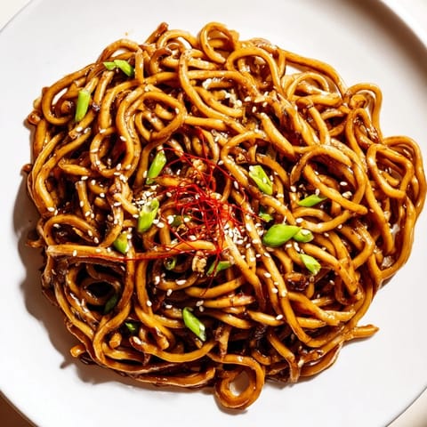 A close-up of a delicious Asian Garlic Noodle Bowl with glistening noodles and fresh green onions.