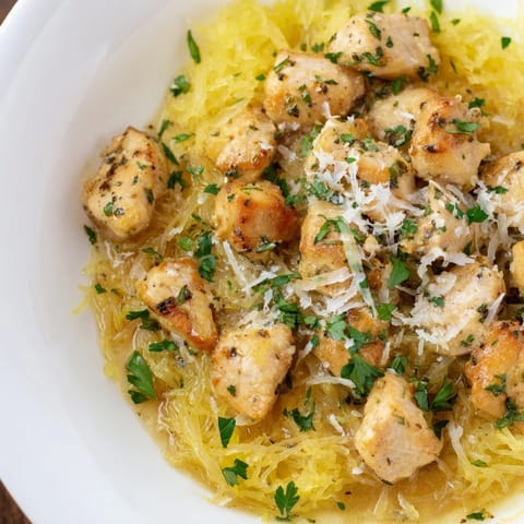 A close-up of bright lemon garlic chicken nestled in fluffy spaghetti squash noodles, garnished with fresh parsley and a light sprinkle of Parmesan cheese.
