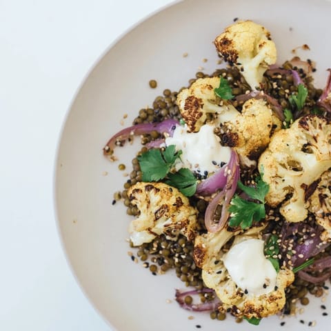 A close-up view of roasted cauliflower with lemon lentils and cumin tahini yogurt, served on a rustic platter with fresh parsley.