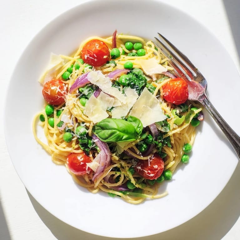 Overhead view of Spring Veggie One-Pot Spaghetti, showcasing colorful vegetables and a light lemon zest garnish on a rustic table.