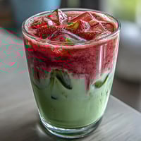 Strawberry Matcha Iced Latte with oat milk, featuring vibrant layers of sweet strawberry puree and earthy green tea, served over ice for a refreshing vegan treat.