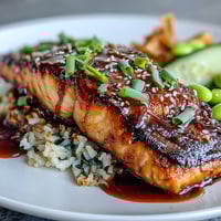 A vibrant teriyaki salmon bowl with fluffy rice, edamame, and crisp cucumber slices, drizzled with savory glaze.